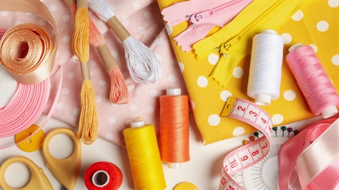 Colorful sewing supplies including thread, fabric, zippers, measuring tape and ribbon