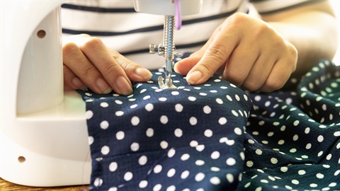 Person using a sewing machine to stitch dark fabric with white polka dots